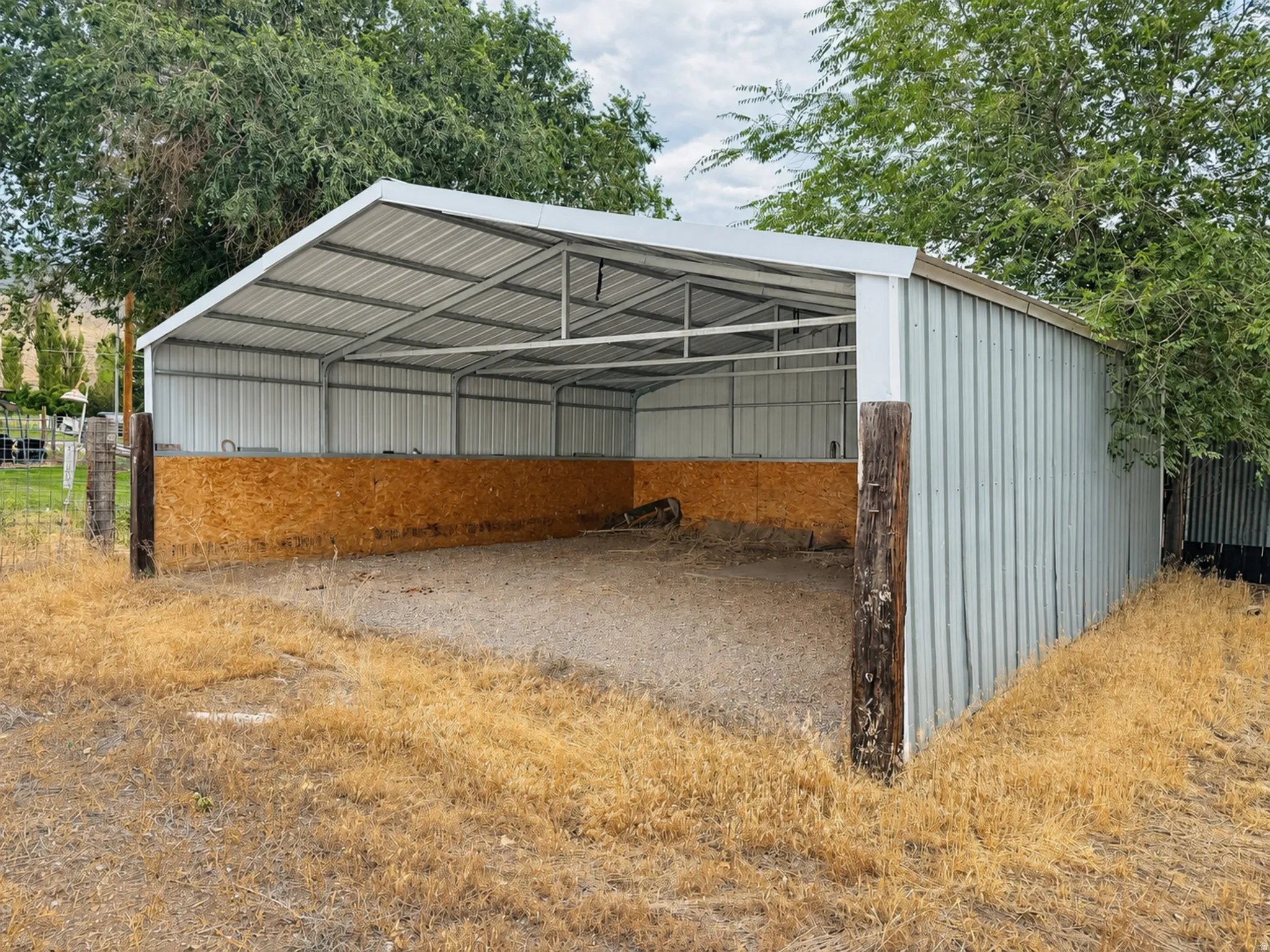 Open-sided metal structure featuring a corrugated roof, metal siding, and a partial wood-paneled interior wall
