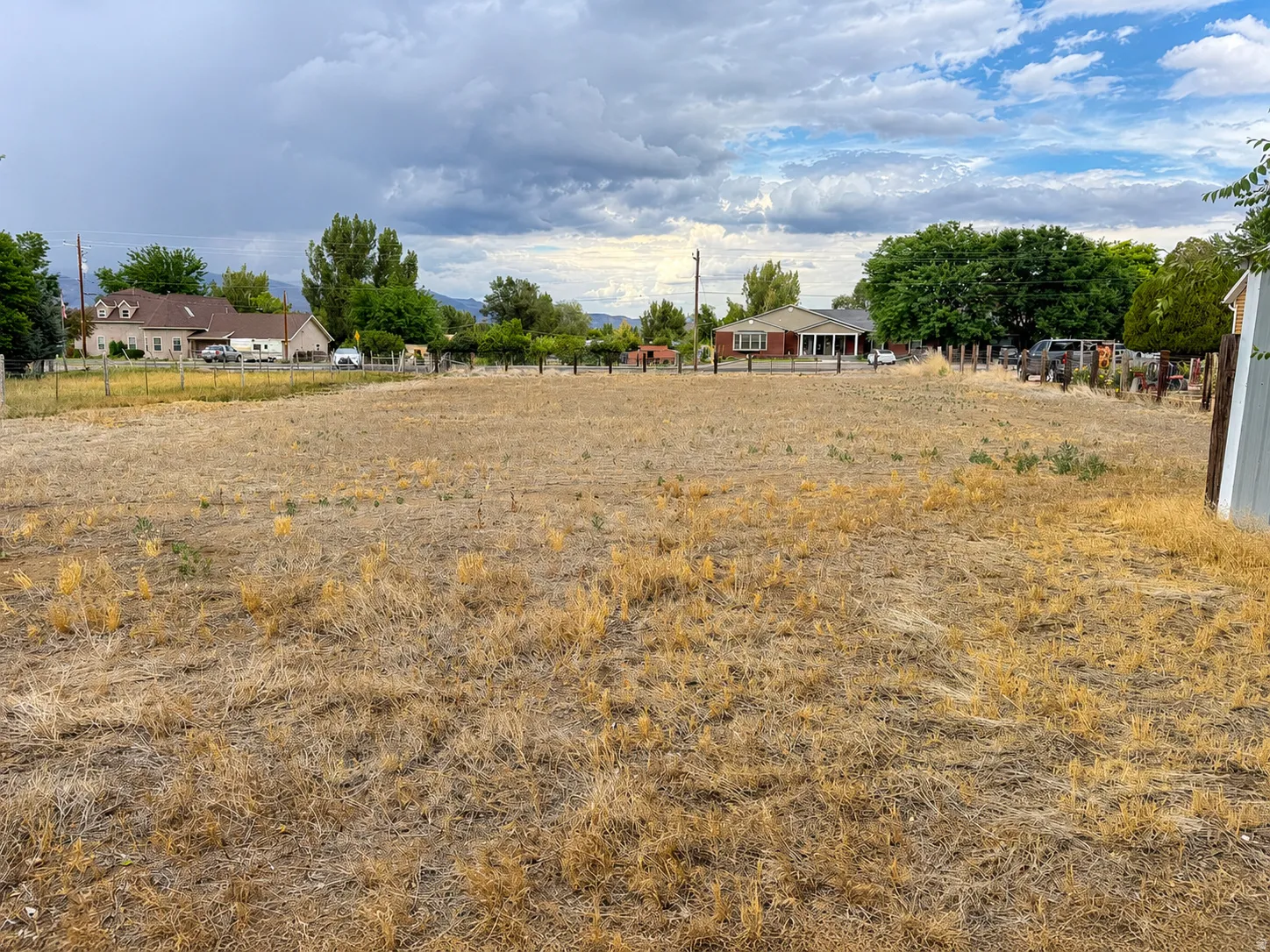 Expansive land parcel with surrounding residential properties, partial fencing, and distant mountain backdrop