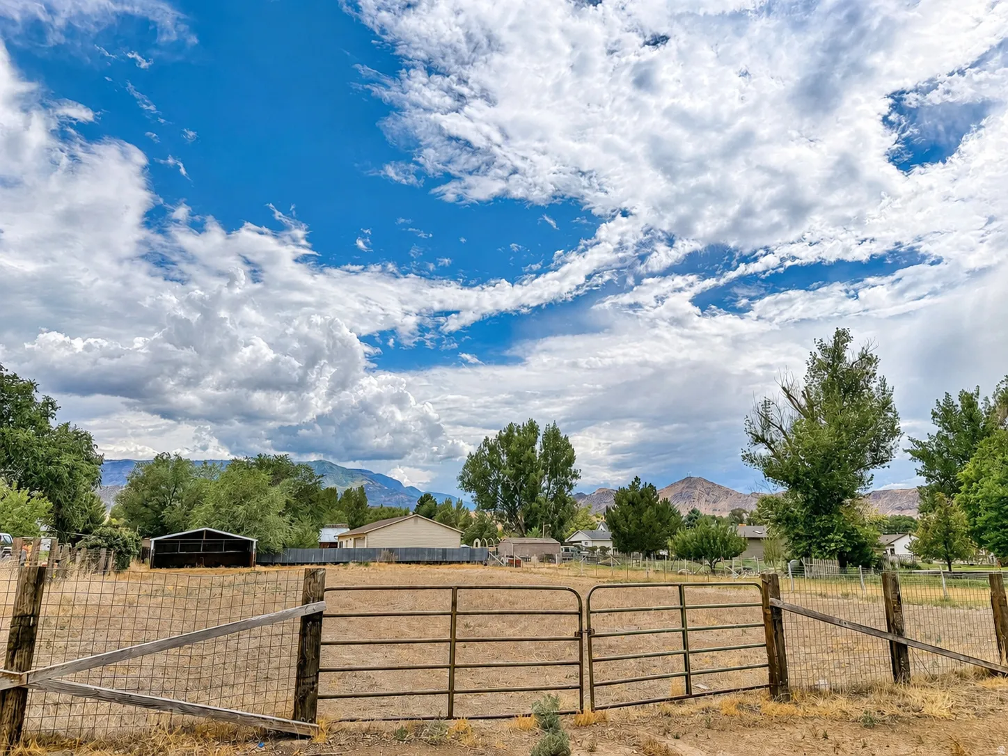 Gated fenced perimeter enclosing an expansive open lot, featuring distant mountain scenery and mature trees