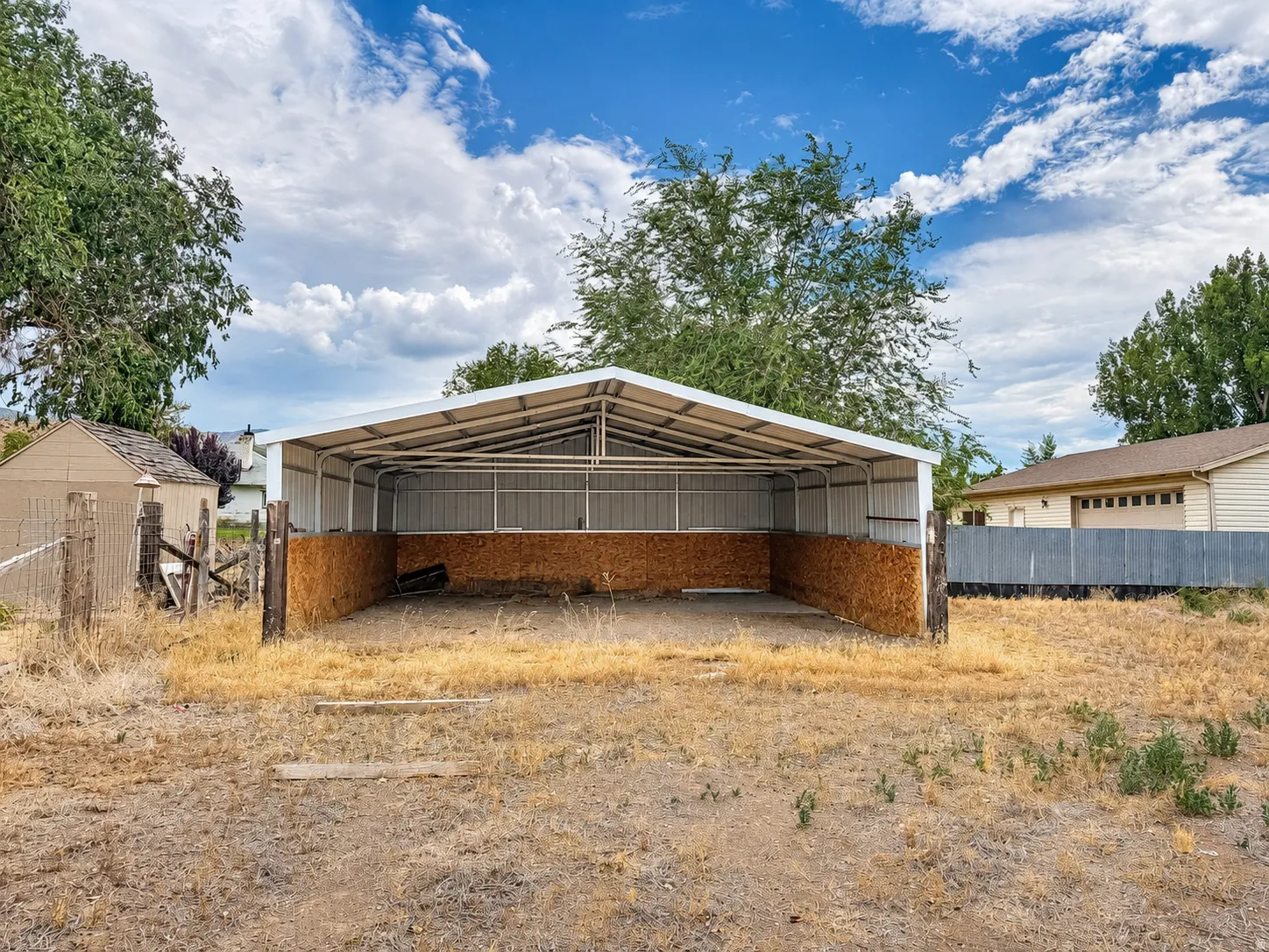 Open-sided metal structure with a gabled roof, partial wood paneling, and a gravel floor