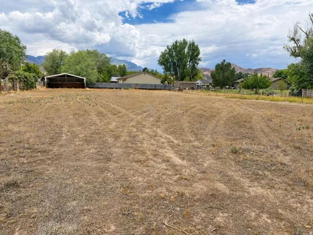 Expansive open lot featuring a metal-roofed outbuilding, mature perimeter trees, and distant mountain scenery