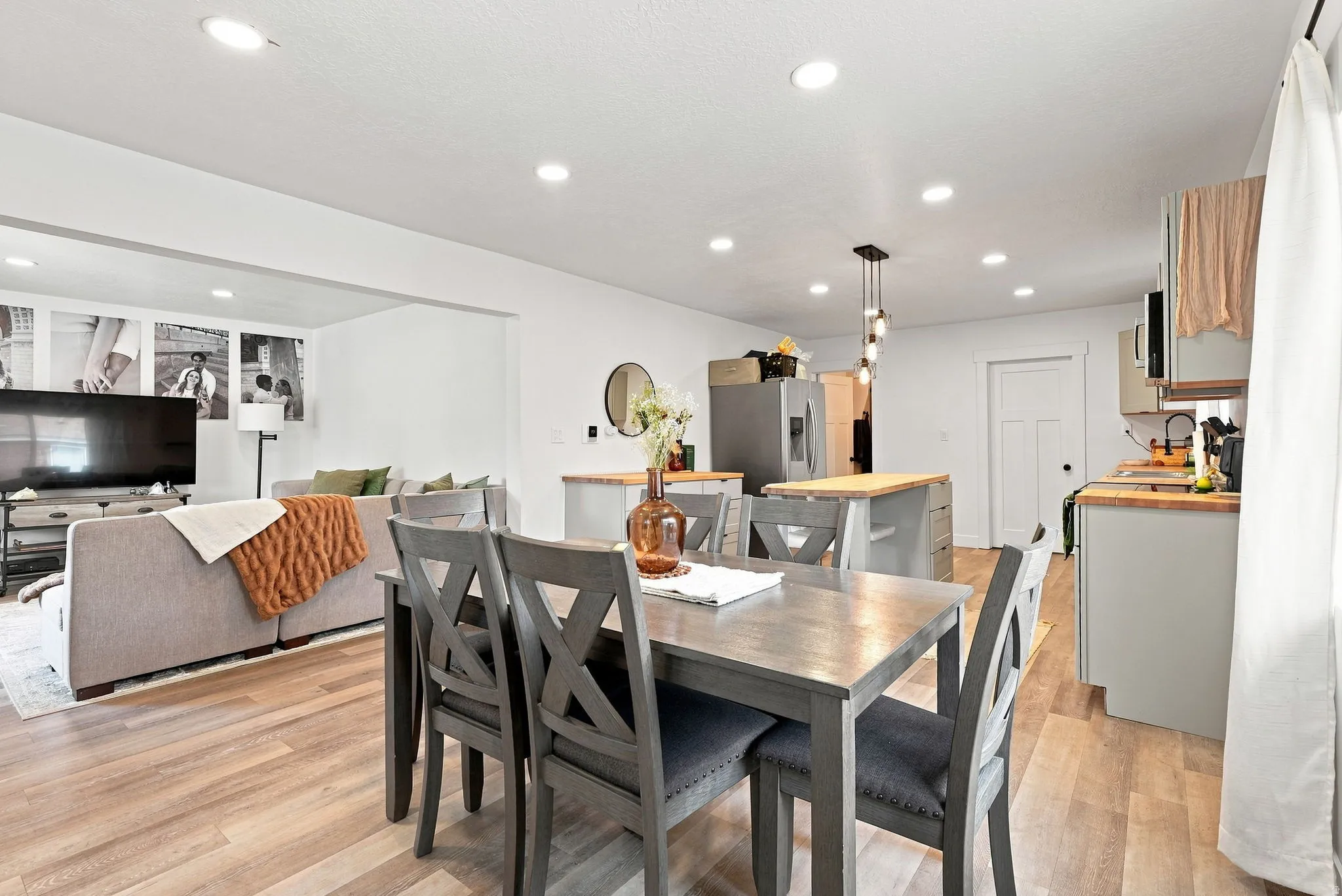 Open-concept living area featuring a wood-finish dining table with seating for four, pendant lighting above, and seamless integration with the kitchen