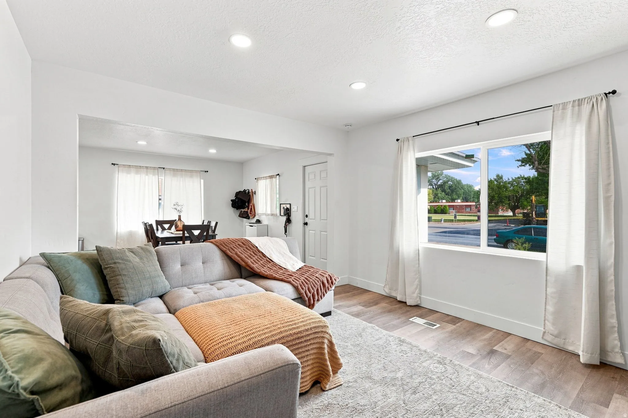 Bright, open-concept living area featuring recessed ceiling lighting, large sliding glass doors with operable windows framing outdoor scenery, wood-finish flooring throughout, and neutral wall finishes