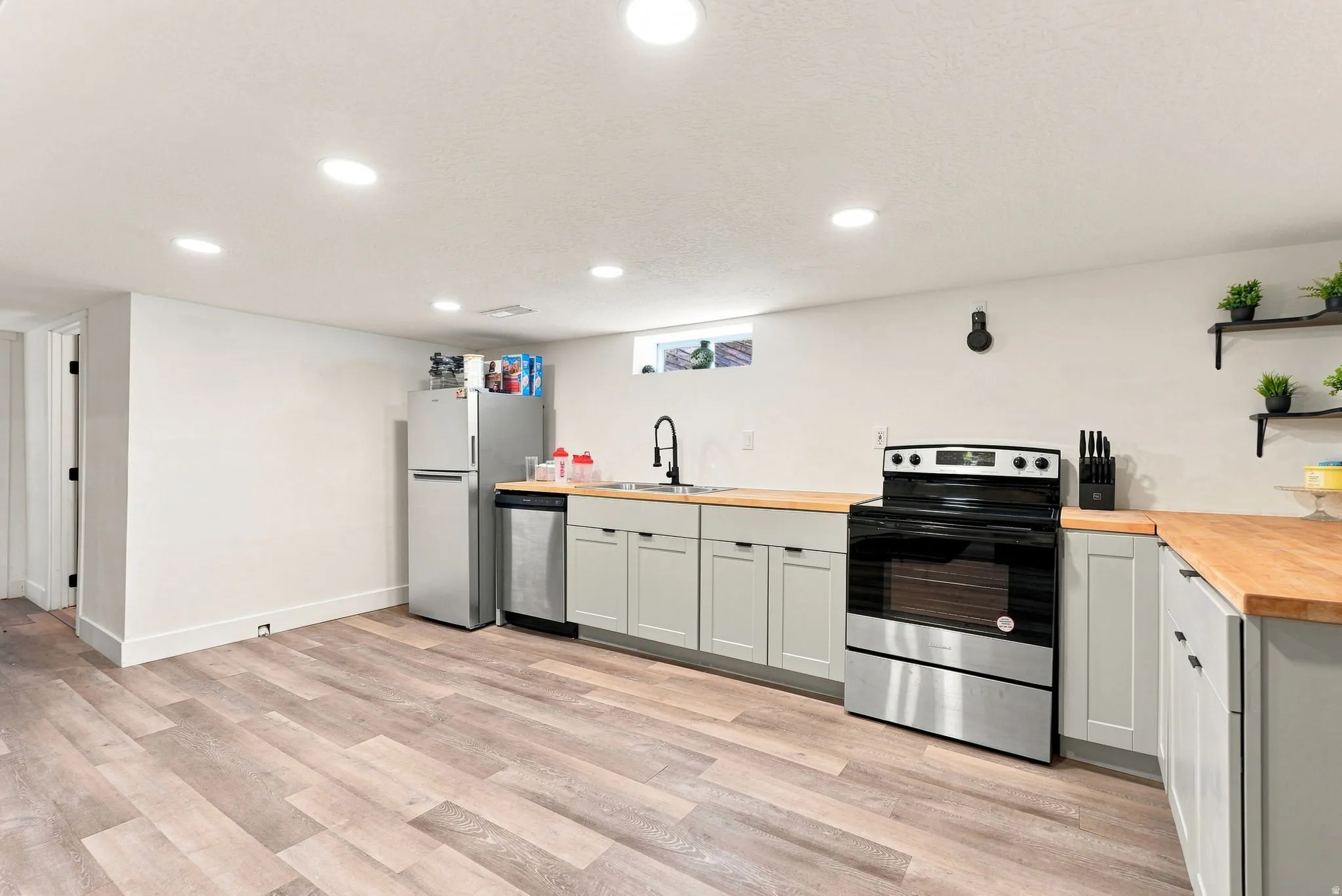 Wood-finish flooring, recessed lighting, light gray cabinetry, wood-finish countertops, and stainless steel appliances