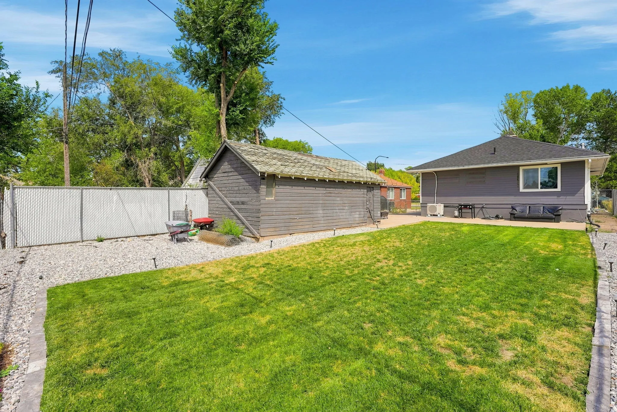 Expansive backyard featuring a manicured lawn, a detached storage building, and a chain-link fence