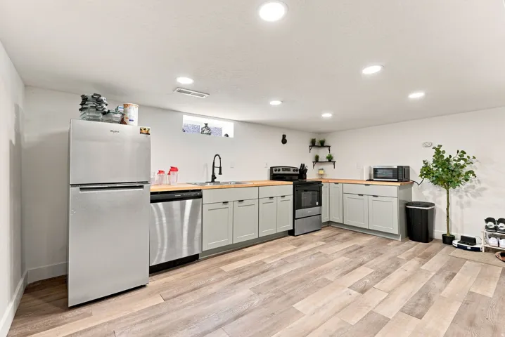 Modern kitchen featuring stainless steel appliances, white cabinetry with ample storage, black countertops, a center island with seating, recessed and pendant lighting, wood-finish flooring, and a bright, open layout with dedicated spaces for cooking and