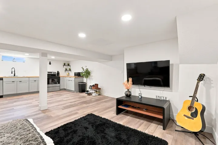 Open-concept living space featuring wood-finish flooring throughout, recessed ceiling lighting, and a wall-mounted flat-screen television above a dark wood media console