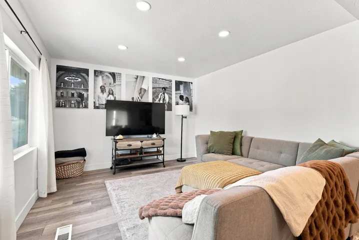 Bright, open living space featuring recessed ceiling lighting, wood-finish flooring throughout, and a wall-mounted flat-screen television on an entertainment stand