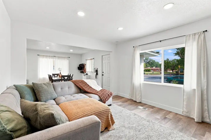 Bright, open-concept living area featuring recessed ceiling lighting, large sliding glass doors with operable windows framing outdoor scenery, wood-finish flooring throughout, and neutral wall finishes