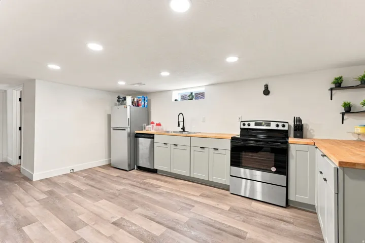 Wood-finish flooring, recessed lighting, light gray cabinetry, wood-finish countertops, and stainless steel appliances