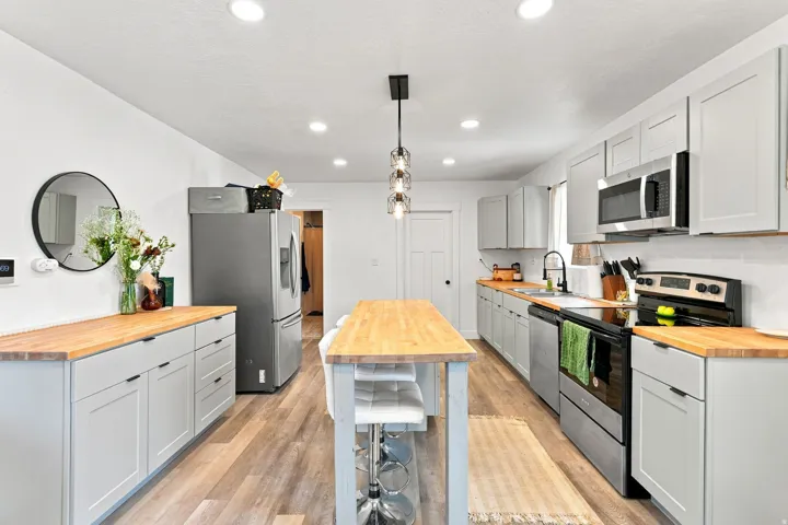 Kitchen featuring wood-finish flooring, light grey cabinetry, butcher block countertops, stainless steel appliances, and a central island with seating