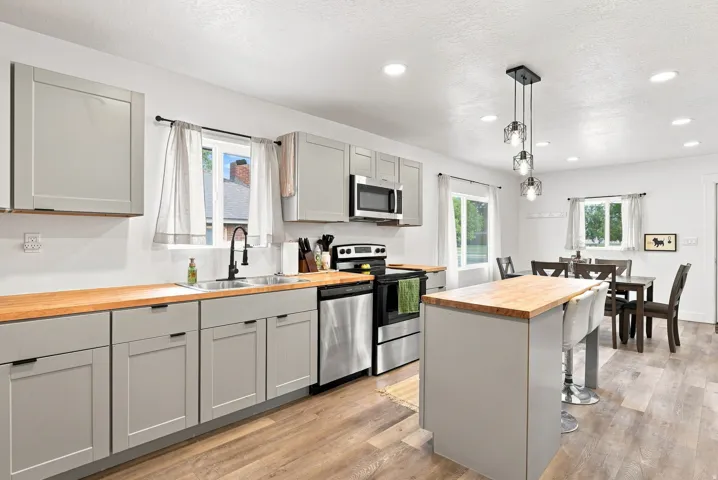 Kitchen featuring light-toned cabinetry, wood-finish countertops, stainless steel appliances, a center island with seating, and wood-finish flooring