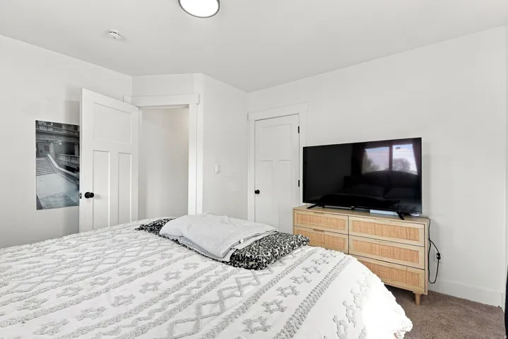Spacious primary bedroom featuring neutral décor, wood-finish dresser with integrated media storage, recessed ceiling lighting, and direct access to multiple closets