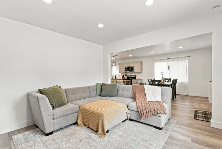 Recessed lighting illuminates the open living area, featuring light wood-finish flooring and a neutral color palette