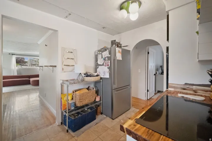 Archway entrance, wood-finish countertop, tile flooring, stainless steel refrigerator, and recessed lighting