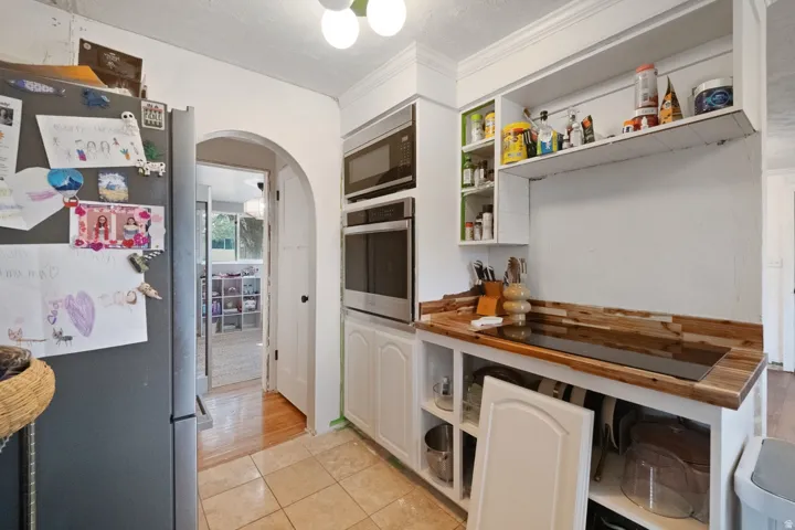 Built-in stainless steel appliances, wood-finish countertops, tiled flooring, arched doorway, and recessed shelving