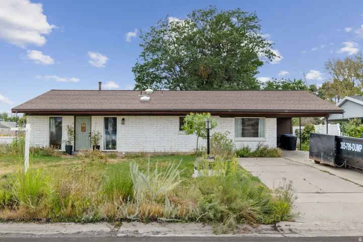 White brick exterior with a brown shingle roof, covered entry, and an attached carport