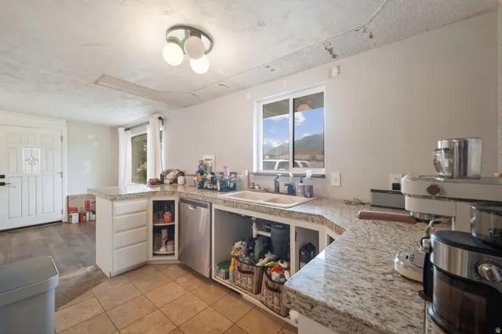 Kitchen featuring white cabinetry, light-toned countertops, a double basin sink, and tile flooring