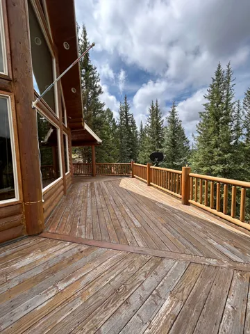 Expansive wood deck with a log railing, featuring a log cabin exterior and large windows