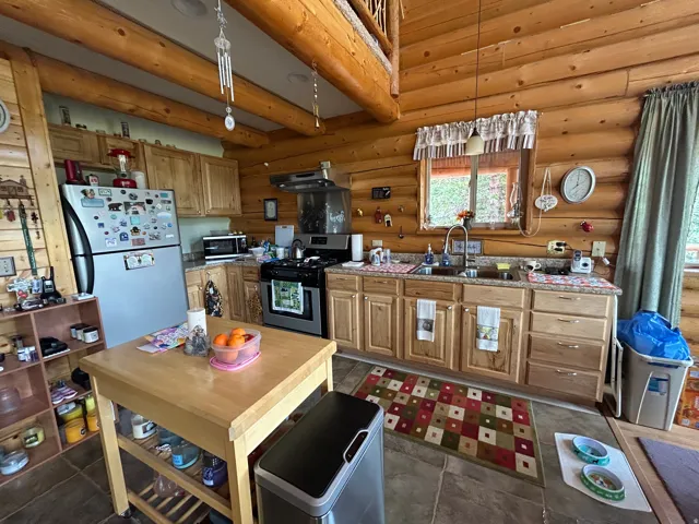 Log cabin interior with exposed wood beams, wood paneling, wood cabinetry, built-in stainless steel appliances, and a double basin sink