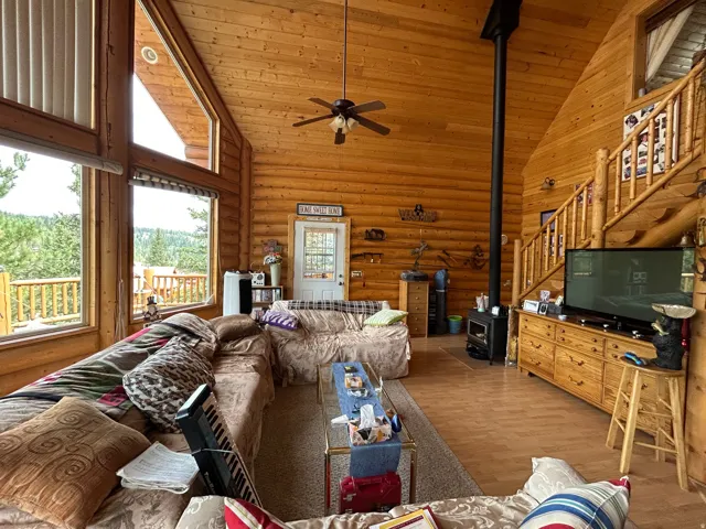Vaulted ceilings with exposed wood beams, extensive natural wood wall paneling, large picture windows, wood-finish flooring, and a wood-burning stove with a stovepipe