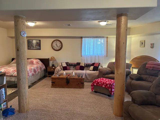 Carpeted room with exposed log columns, recessed lighting, and a single window with white curtains