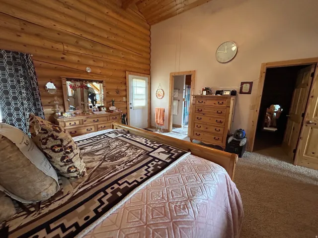 Log wall construction with a vaulted ceiling, wood-framed interior doors, and a white exterior door