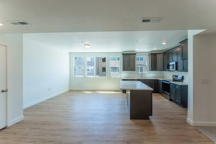 Open-concept living space featuring wood-finish flooring, a kitchen island with seating, dark shaker-style cabinetry, and stainless steel appliances