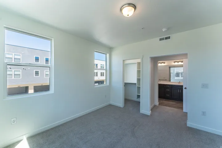 Light-colored walls, two windows, carpeted flooring, built-in closet with shelving, and an en-suite bathroom with a dark wood vanity