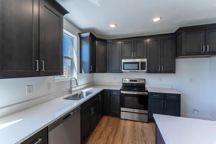 Dark wood-finish cabinetry with modern pulls, stainless steel appliances, light-toned countertops, wood-finish flooring, and recessed lighting