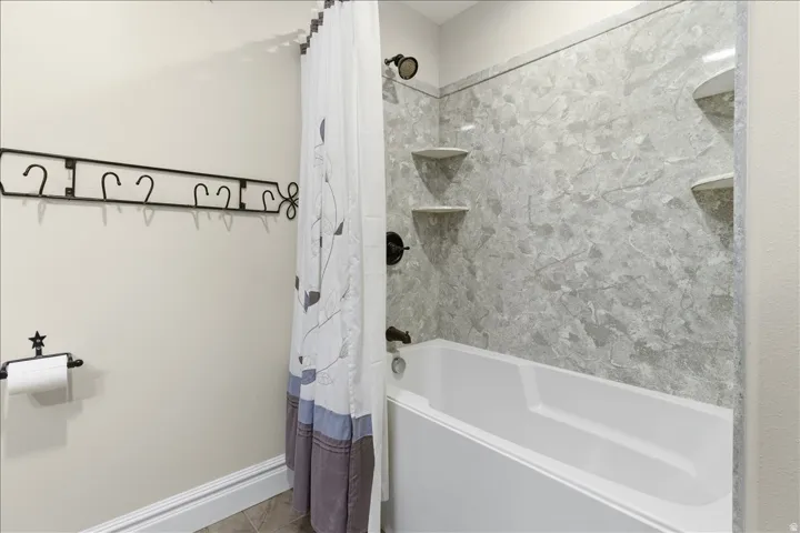 Bathtub with wall-mounted shower, textured grey shower surround, and built-in corner shelving