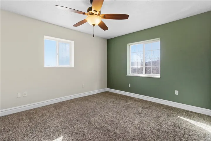 Neutral wall color with an accent wall, two windows, ceiling fan with integrated lighting, and carpet flooring