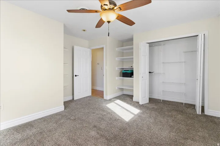 Carpeted flooring, ceiling fan, white bi-fold closet doors, built-in shelving, and white interior doors