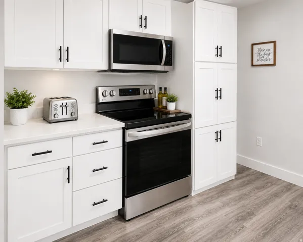 White shaker-style cabinetry with matte black hardware, stainless steel appliances, light-toned countertops, and wood-finish flooring