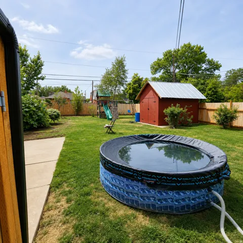 Expansive grassy backyard featuring a paved walkway, wood privacy fencing, and a red storage shed with a metal roof