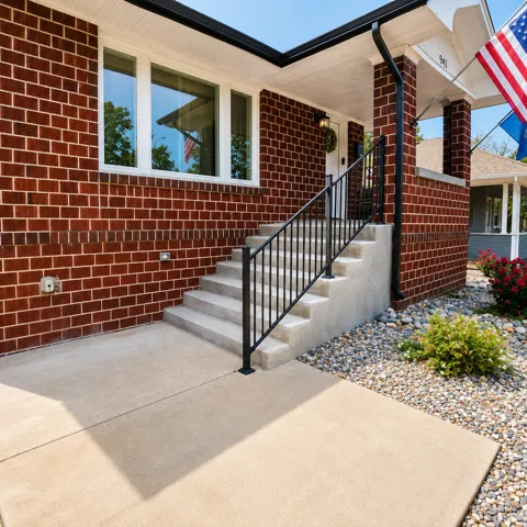 Brick exterior with white trim windows, concrete steps, black metal railing, and a covered entry porch