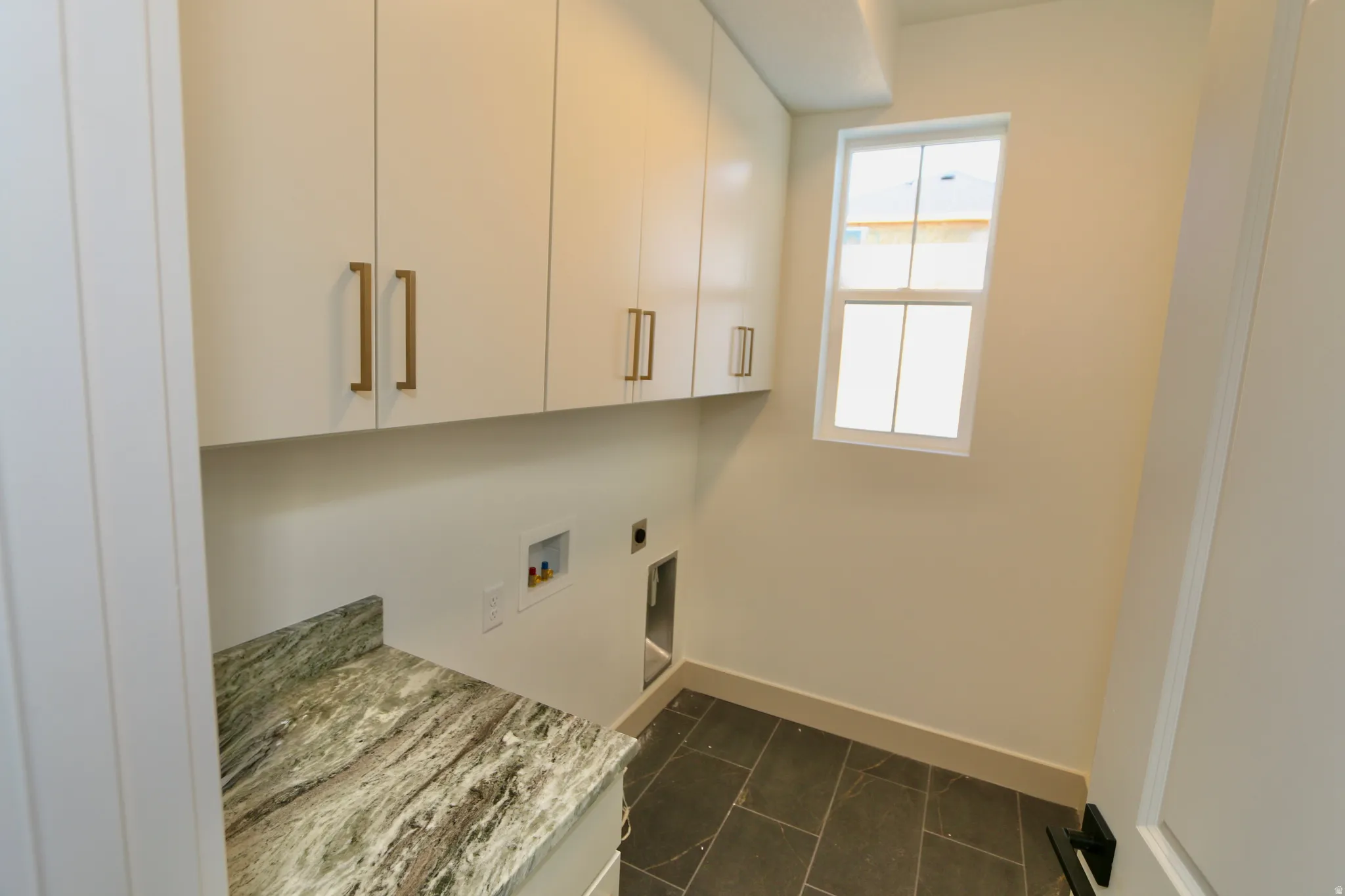 White upper cabinetry with gold-tone hardware, a variegated stone-finish countertop, and a window for natural light
