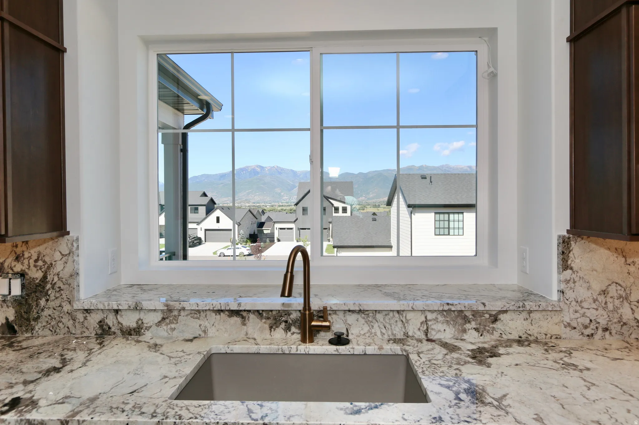 Kitchen sink window with mountain backdrop, undermount sink, stone countertop, and dark wood-finish cabinetry