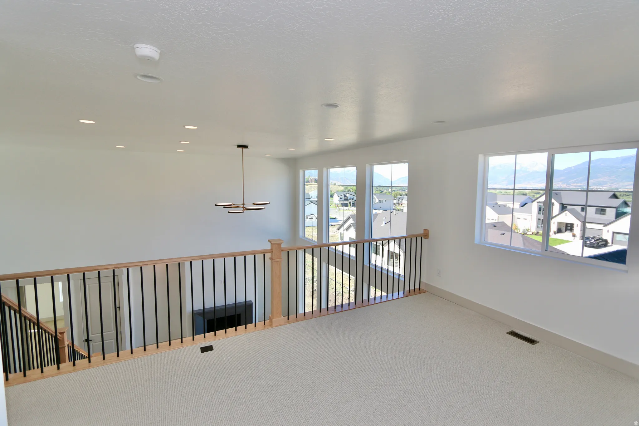 Open concept loft space featuring carpeted flooring, multiple recessed lights, and large windows with mountain scenery