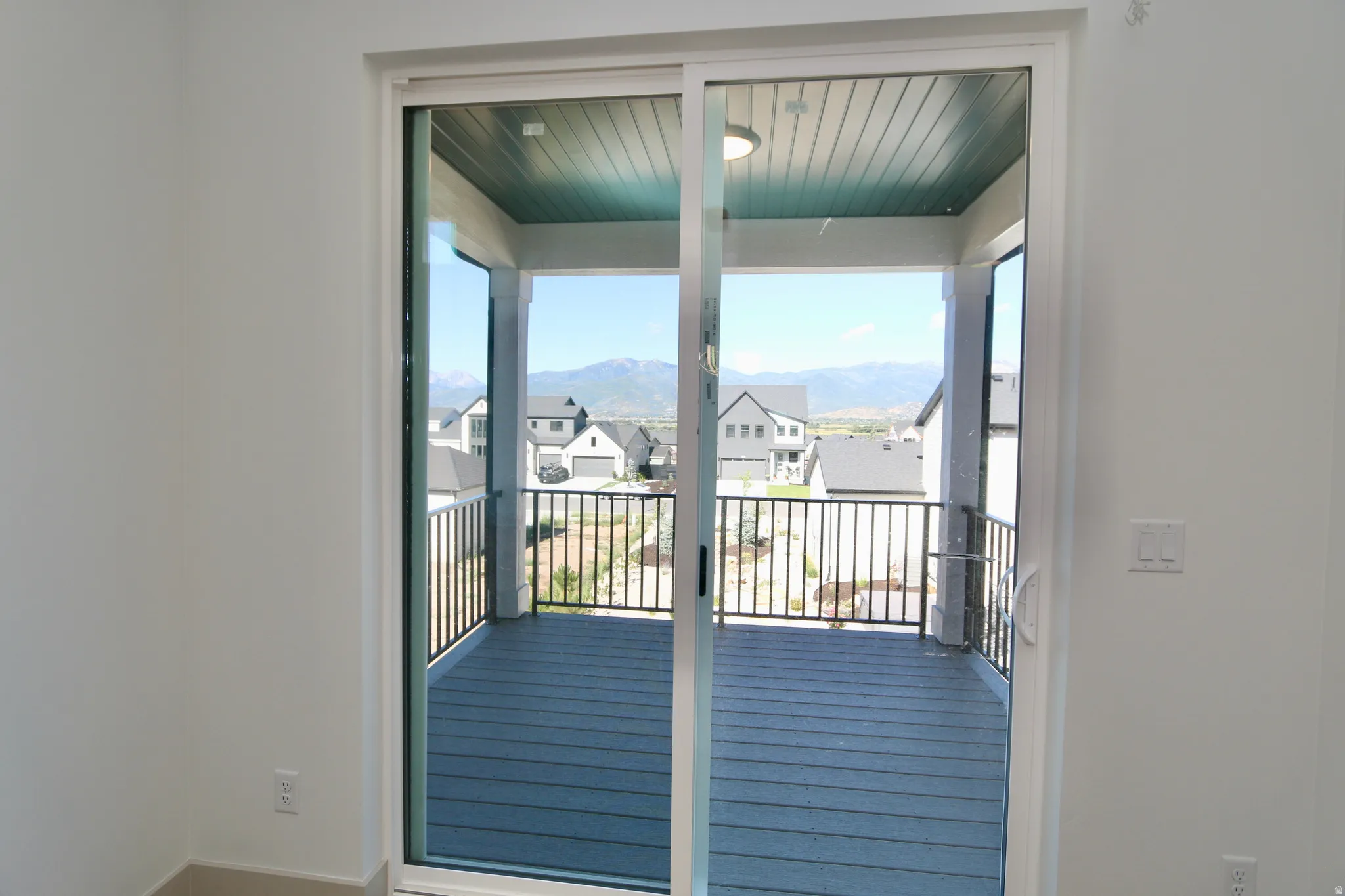Sliding glass doors opening to a covered balcony with a slat ceiling, composite decking, metal railings and gas BBQ connection.