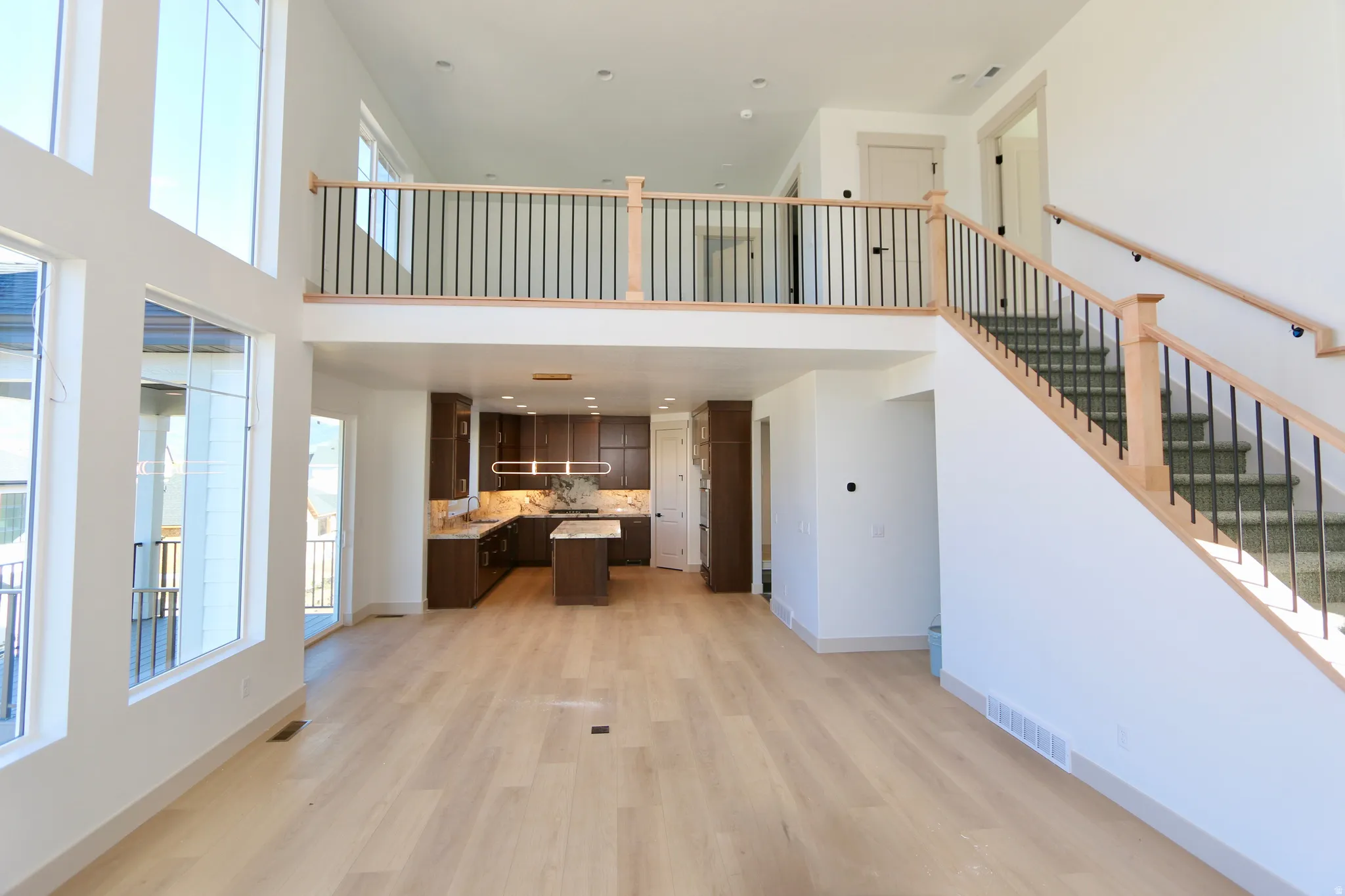 Great room with vaulted ceilings, a wall of windows with valley & mountain views, wood-finish flooring, dark wood cabinetry, a kitchen island, and a staircase with an open railing