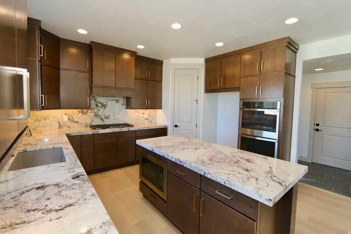 Kitchen featuring wood-finish cabinetry, light-toned stone countertops, a gas cooktop, built-in double ovens, and a built-in microwave