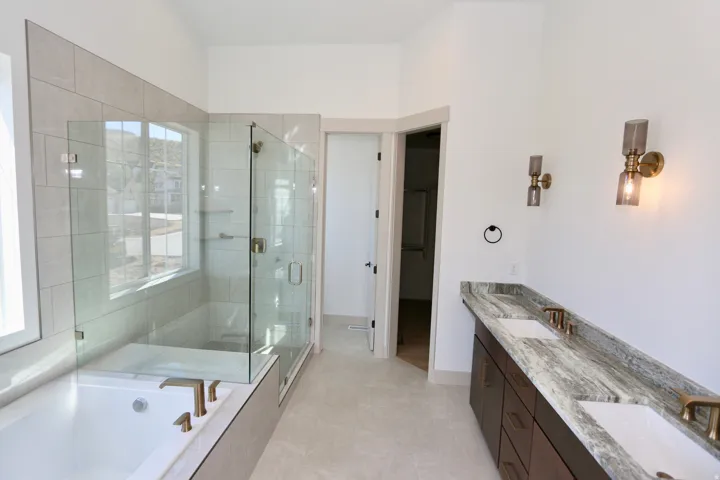 Large master-bath with dual vanity, quartzite countertop, soaking tub, euro-glass-enclosed shower with bench,, wall-mounted light fixtures, and tile flooring