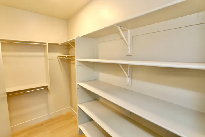 Large master-suite walk-in closet featuring extensive built-in shelving, multiple hanging rods, and light wood-finish flooring