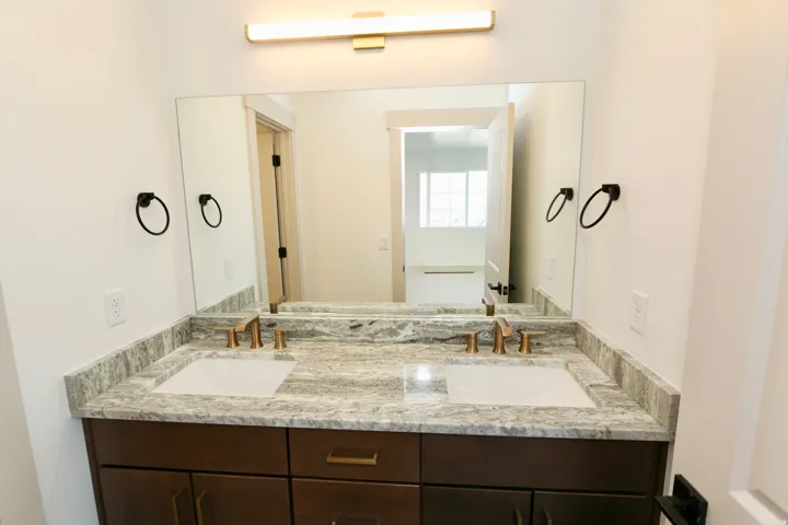 Bathroom #3 with double vanity with undermount sinks, stone countertop, brass-finish faucets, and dark wood-finish cabinetry
