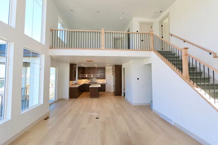 Great room with vaulted ceilings, a wall of windows with valley & mountain views, wood-finish flooring, dark wood cabinetry, a kitchen island, and a staircase with an open railing