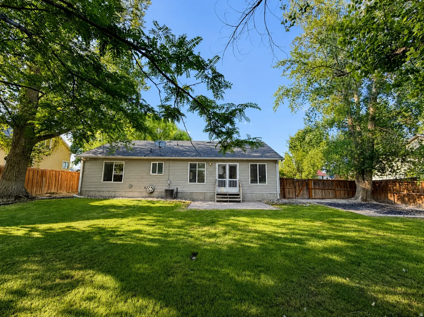 Expansive backyard featuring a lush lawn, mature trees, wood fencing, and a concrete patio