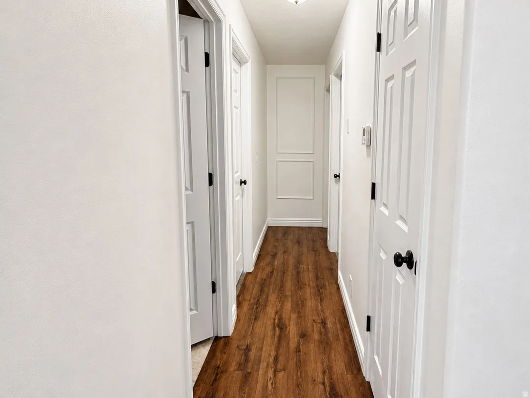 Hallway featuring wood-finish flooring, crisp white walls, and paneled interior doors with dark hardware