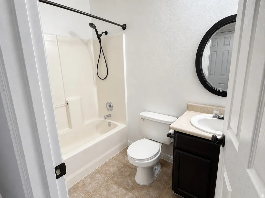 Bathroom featuring tiled flooring, a white bathtub with shower, a vanity with a dark cabinet, and a round wall mirror