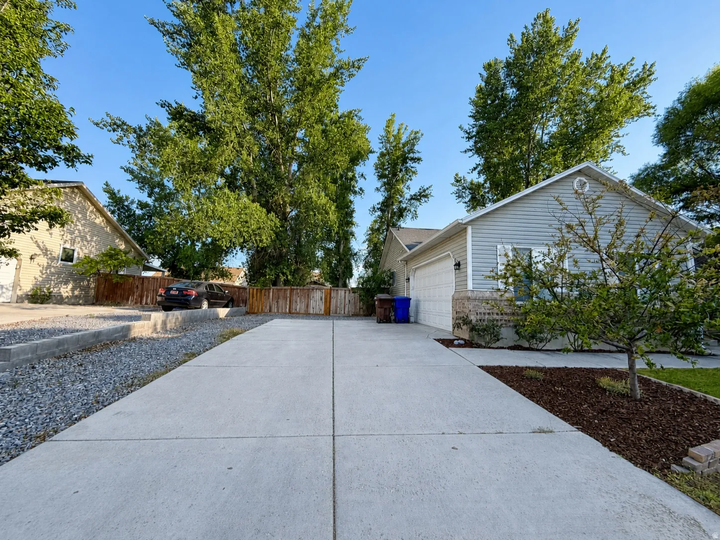 Concrete driveway with an integrated two-car garage, complemented by a wood fence and mature trees